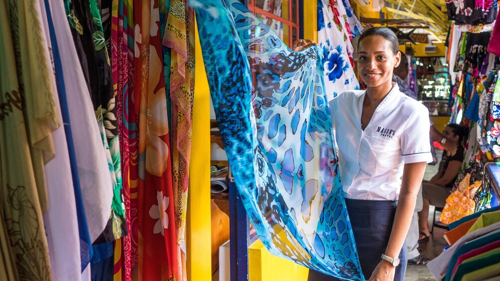 Show item 4 of 5. Tour guide holding up textiles in market in Maha Island