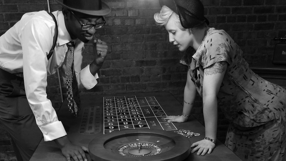 Black and white image of people in vintage clothing looking at a roulette table