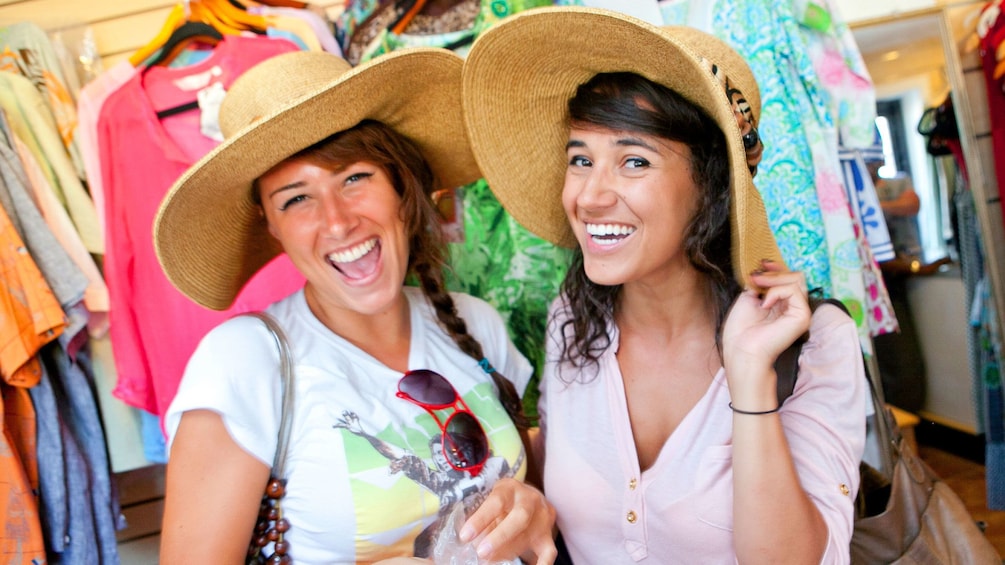 Two women trying on straw hats in a shop in Jamaica