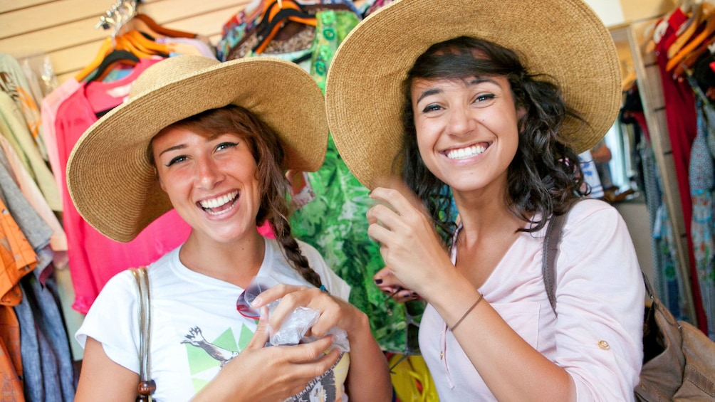Two women trying on straw hats in a shop in Jamaica