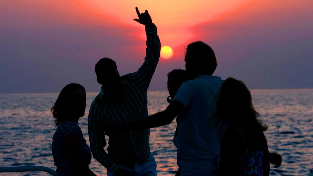 Four silhouetted people dance on a boat at sunset in Jamaica