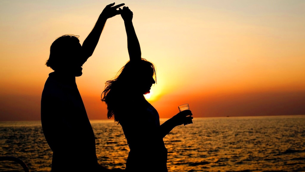 Two silhouetted people dance on a boat at sunset in Jamaica
