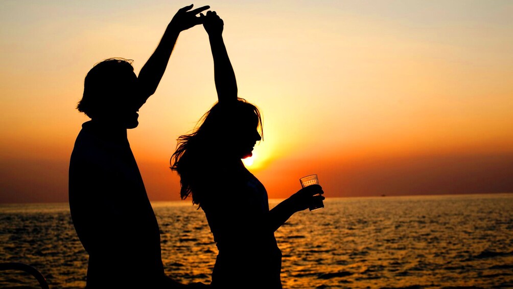 Two silhouetted people dance on a boat at sunset in Jamaica