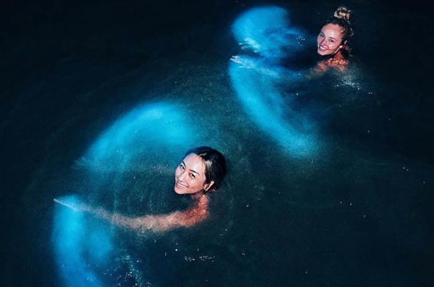 Women swimming in glowing bioluminescent water at night in Puerto Rico