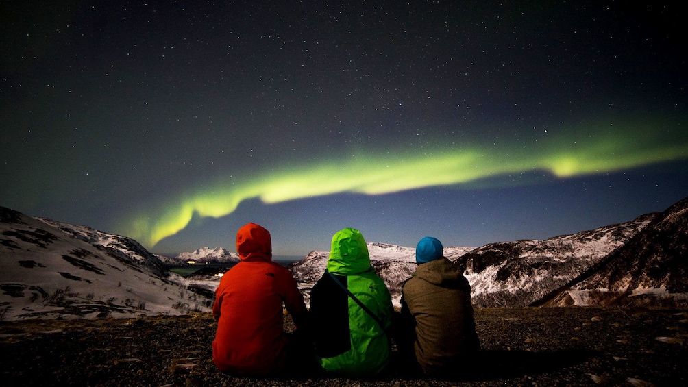 Trio sits watching aurora borealis in Tromso