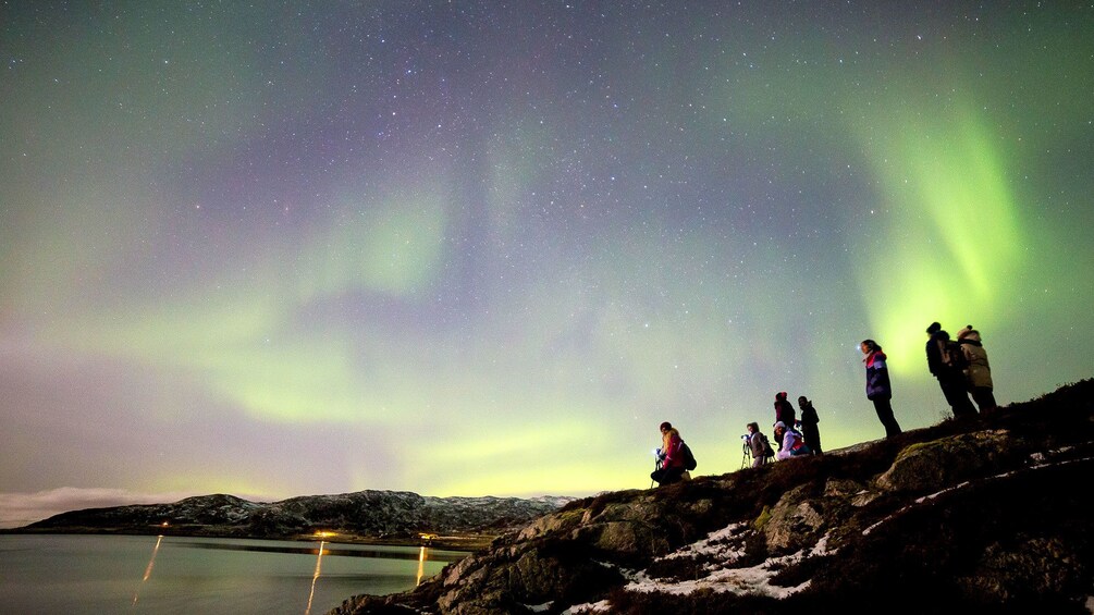 People standing upon ridge to view aurora borealis in Tromso