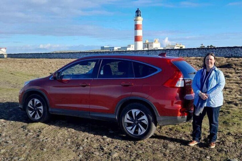 Louise stood next to her red Honda CR-V Car alongside a red and white coloured lighthouse 