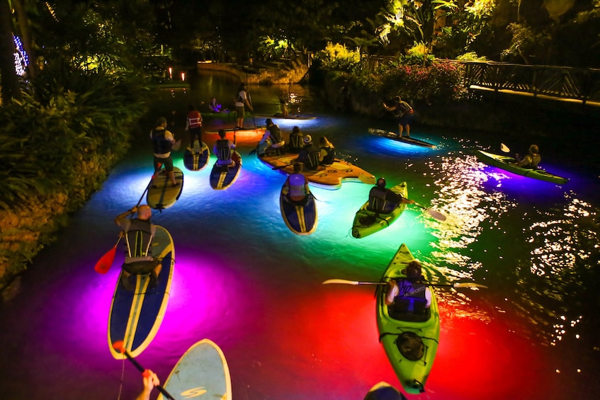 Colorfully illuminated pool at night with paddleboarders 