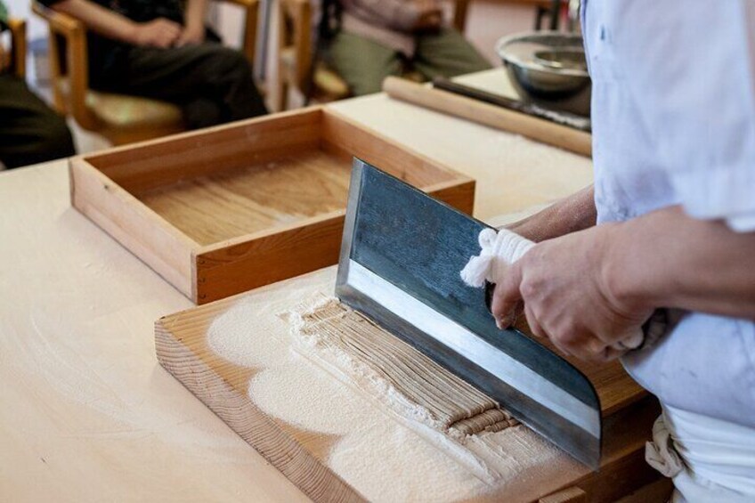 Using a large soba knife, finely slice the soba noodles.