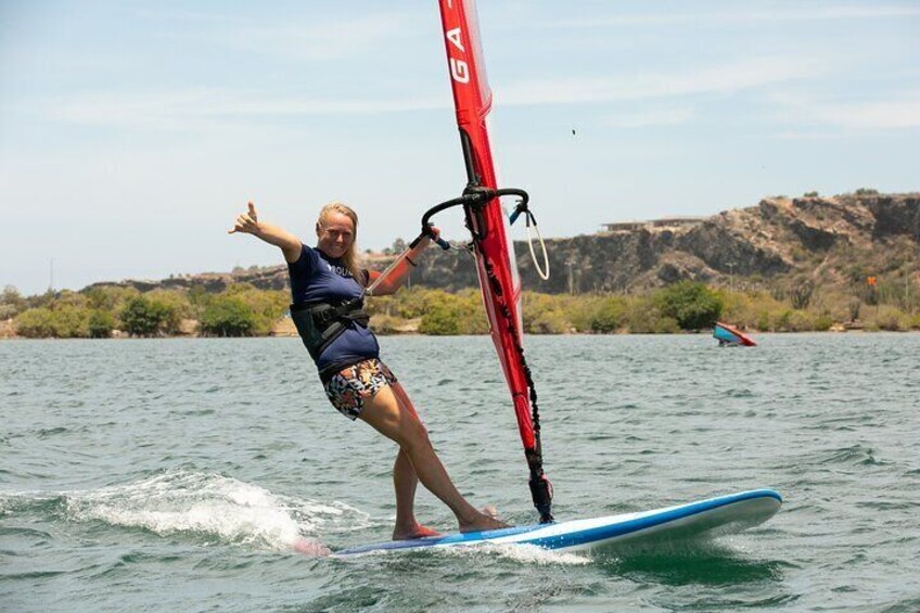 A confident woman windsurfs on the serene Spanish Waters, showcasing her skills learned from our expert instructors.