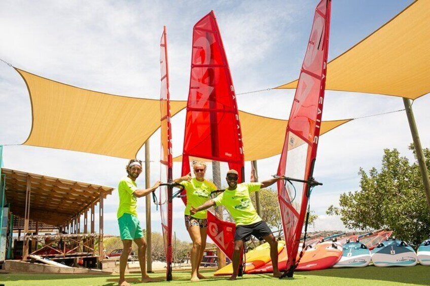 Meet our passionate crew, posing with windsurfing sails and boards, dedicated to making your windsurfing experience unforgettable