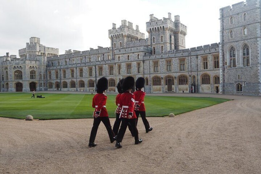 Guardsmen in iconic red uniforms and bearskin hats march through the historic grounds of Windsor Castle, a symbol of British tradition and pageantry.