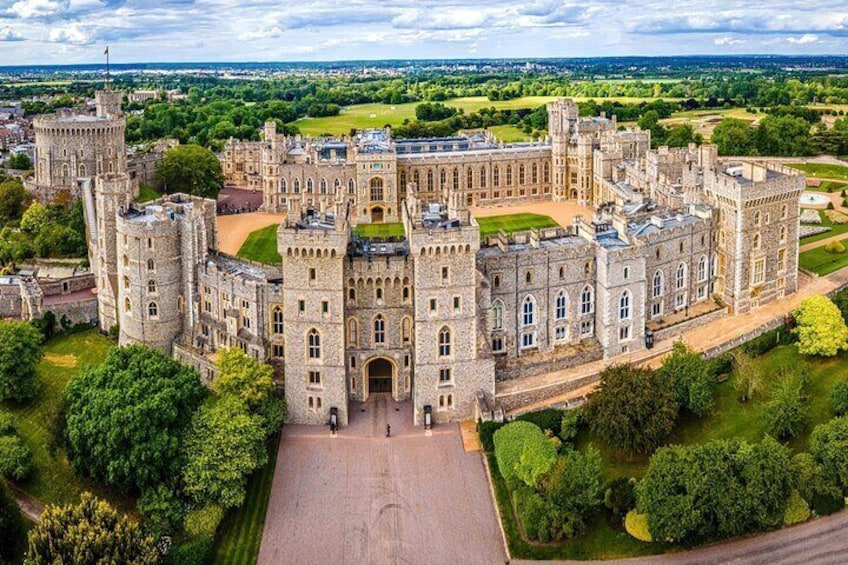 An aerial view of Windsor Castle, showcasing its grand medieval architecture and sprawling grounds, surrounded by lush greenery.