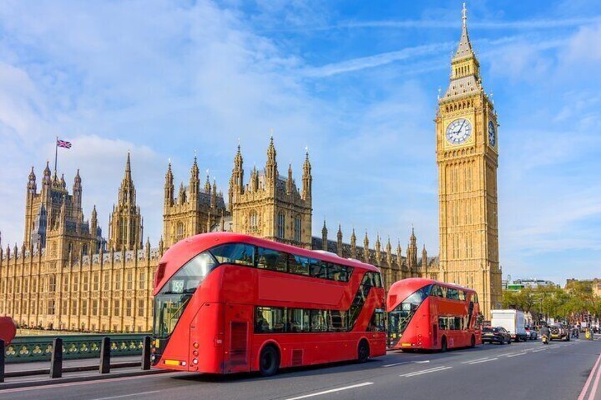 Red double-decker buses pass by the Houses of Parliament and Big Ben on Westminster Bridge, an iconic scene of London’s rich heritage.