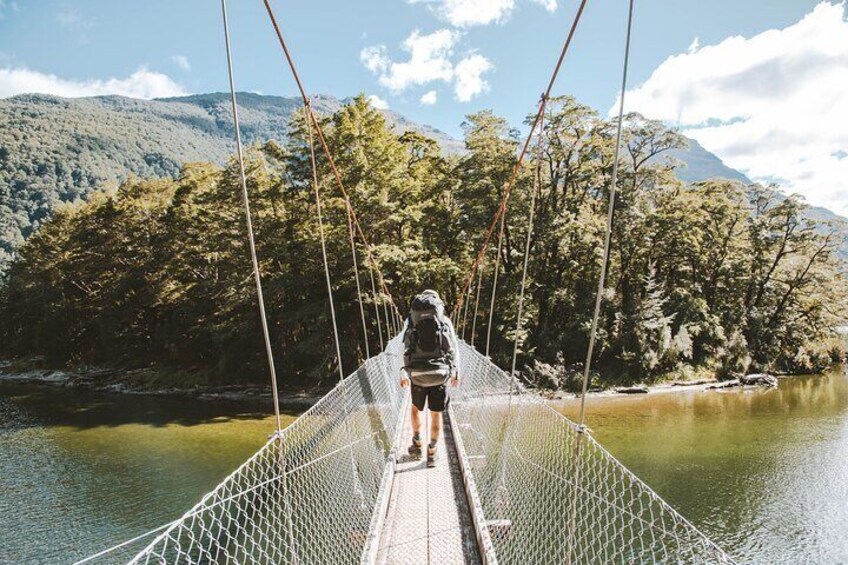 Hiker crossing the swing bridge across the Clinton River, Milford Track.