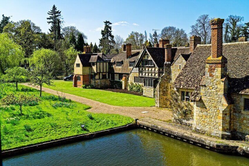 A peaceful view of the charming Tudor-style cottages within the grounds of Hever Castle, nestled beside a serene canal and surrounded by lush greenery.