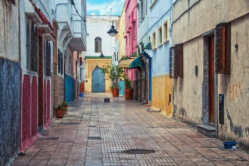 Tranquil scene of a winding street in the Medina of Rabat, showcasing traditional Moroccan architecture with whitewashed walls and colorful accents.