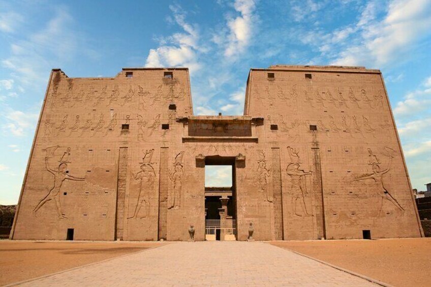 A photo of the facade of the Temple of Horus in Edfu, showcasing the massive pylons, decorated with hieroglyphs, and the columns leading into the temple.