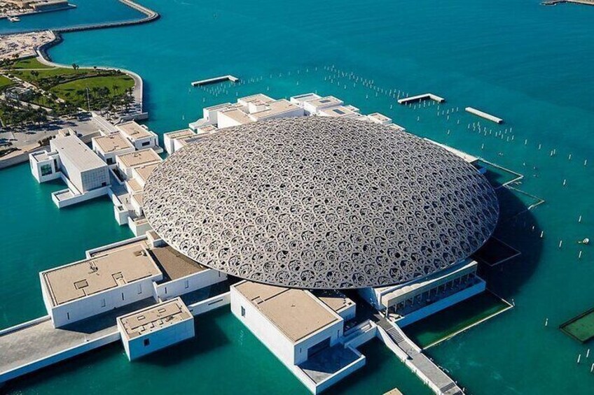An aerial view of the iconic Louvre Abu Dhabi dome, showcasing its intricate geometric design that reflects sunlight onto the museum's surrounding waters.