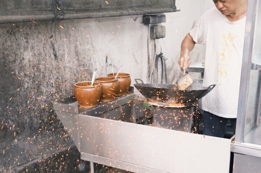 Char koay teow frying over a charcoal fire, capturing the perfect wok hei for that authentic smoky flavor.