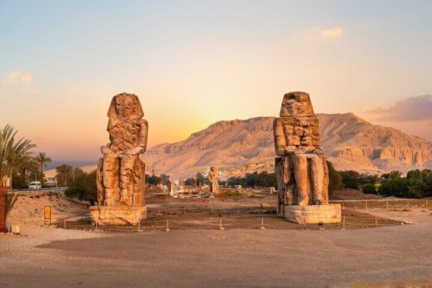 The Colossi of Memnon, two iconic statues of Pharaoh Amenhotep III, set against the stunning backdrop of the Egyptian desert and the Nile River.