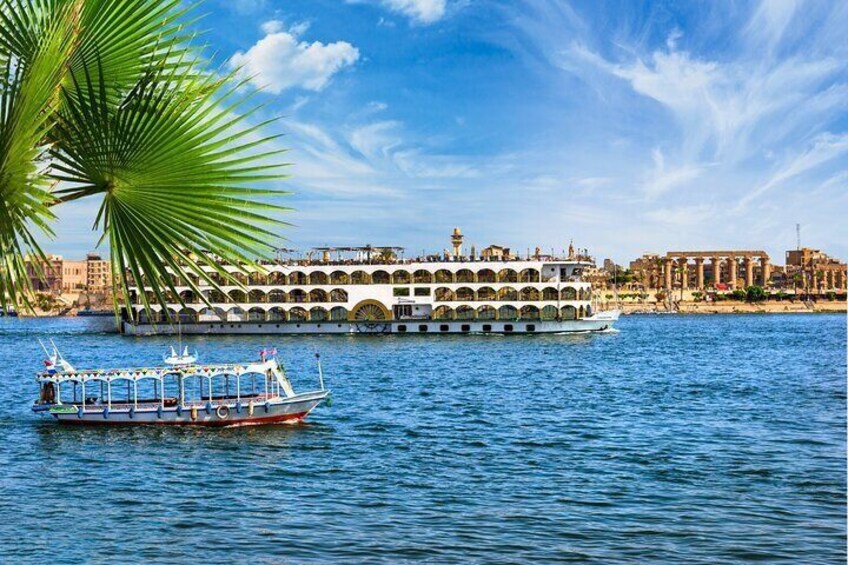 A scenic view of a Nile cruise ship sailing past ancient temples in Luxor