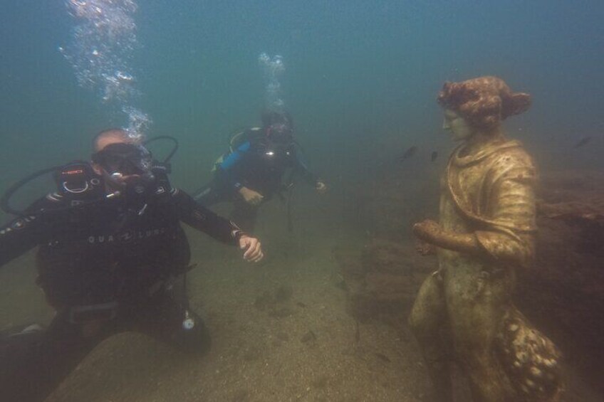 Two divers admire one of the statues of Dionysius of Claudius' Nymphaeum, on a day with bad visibility