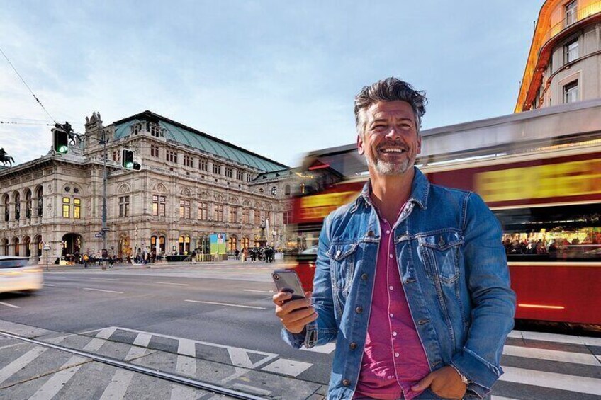 Cheerful man with smartphone in front of the Vienna State Opera while a red tram passes dynamically.