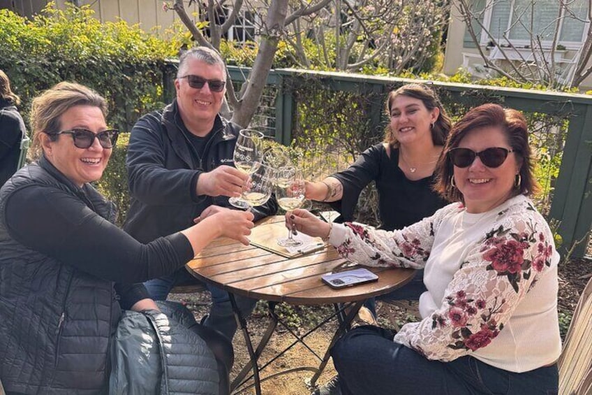 A group of friends toasting with wine glasses at an outdoor winery patio, enjoying a sunny afternoon during the Santa Ynez Full-Day Wine Experience.