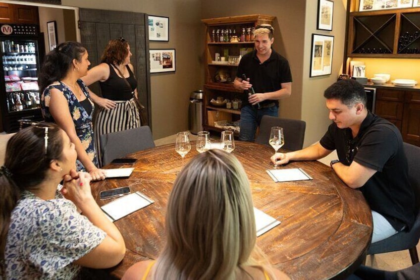A wine-tasting session inside a cozy Santa Ynez tasting room, where guests gather around a rustic wooden table to sample premium wines and learn from an expert host.