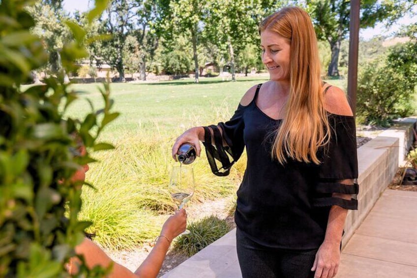 A winery host pouring red wine for a guest during a tasting stop on the Santa Ynez Full-Day Wine Experience, surrounded by beautiful vineyard scenery.