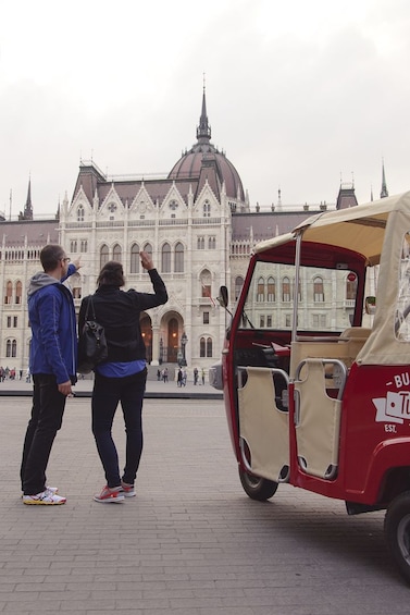 Couple near their Tuk Tuk vehicle looking at historical building in Budapest