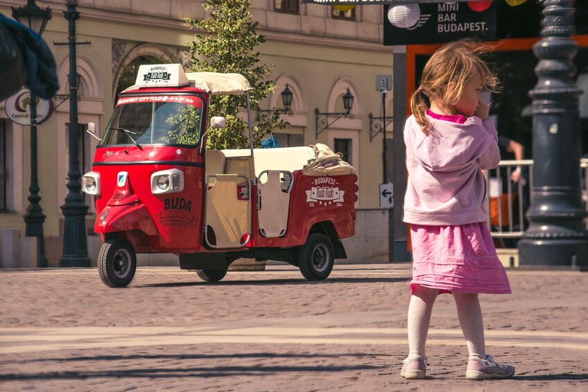 Little girl with Tuk Tuk vehicle in the background on the street in Budapest