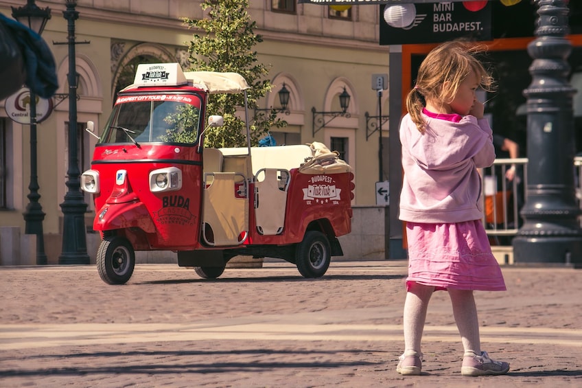 Little girl with Tuk Tuk vehicle in the background on the street in Budapest