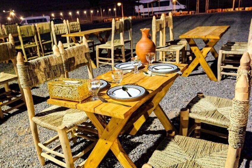 Experience the charm of a traditional Moroccan dinner under the open sky in the serene Agafay Desert. Beautifully set wooden tables and handwoven chairs create an inviting and authentic ambiance, perf