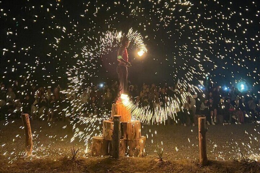 Prepare to be amazed by a stunning fire show that lights up the night in the Agafay Desert. The performer, standing atop wooden pillars, spins fiery tools to create mesmerizing patterns of sparks, cap