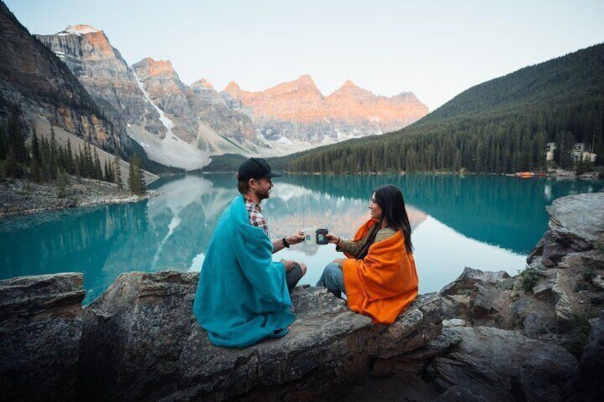 Couples enjoying the sunrise at Moraine Lake with hot drinks and cozy blankets.