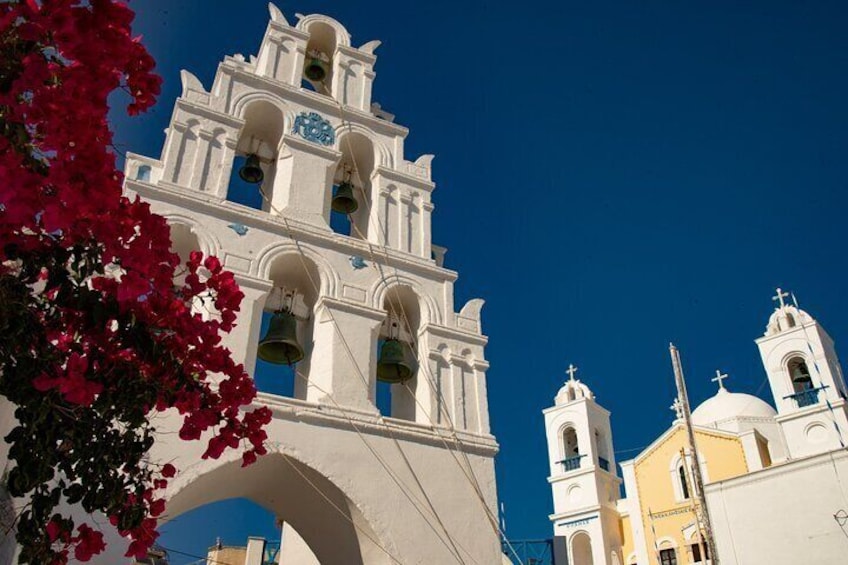 The bell tower of Megalochori, Santorini, framed by vibrant bougainvillea.