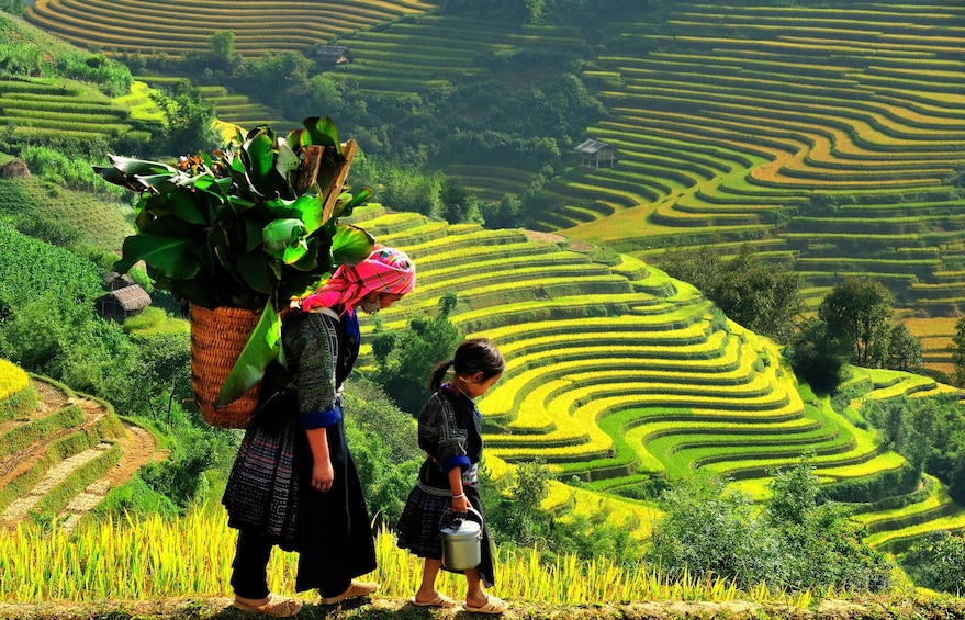 Woman and girl carry baskets and tins through Sapa Valley in Vietnam