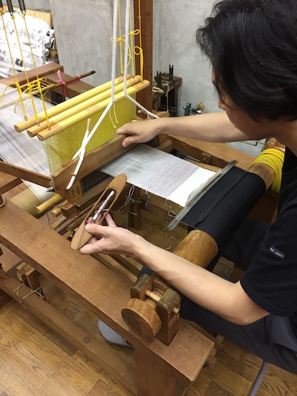 Woman works on loom to create silk fabric at  Koho Nishiki Textile Studio in Kyoto, Japan