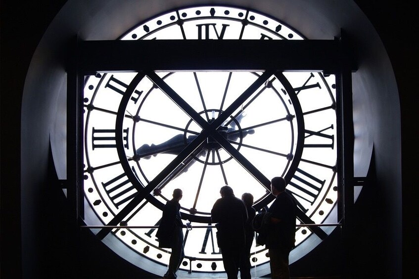 Silhouetted people stand next to a clock