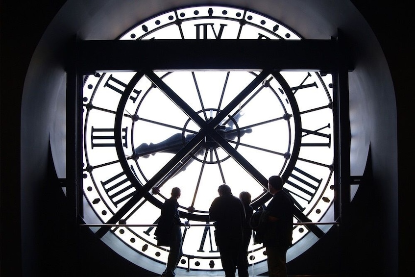 Silhouetted people stand next to a clock