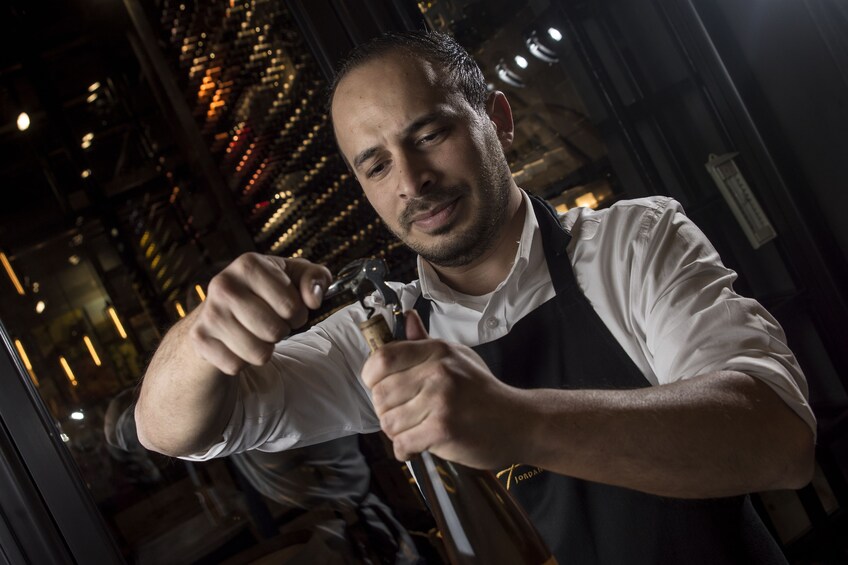 Man opening a bottle of wine at a wine tasting bar in Amman