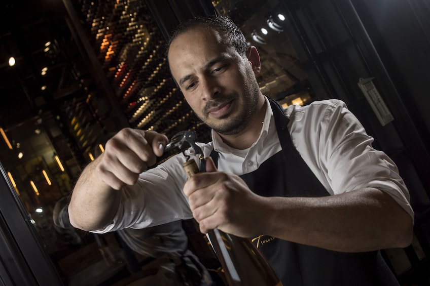Man opening a bottle of wine at a wine tasting bar in Amman
