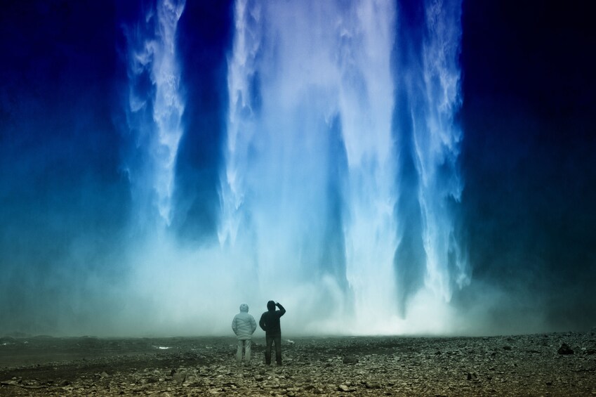 Silhouetted people walk under a waterfall in Iceland