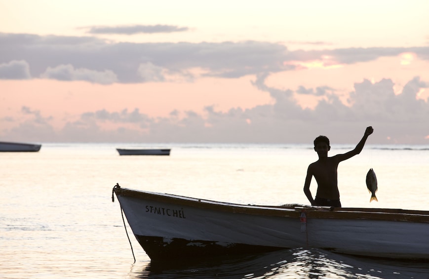 Young man on a boat holding up a caught fish in Mauritius