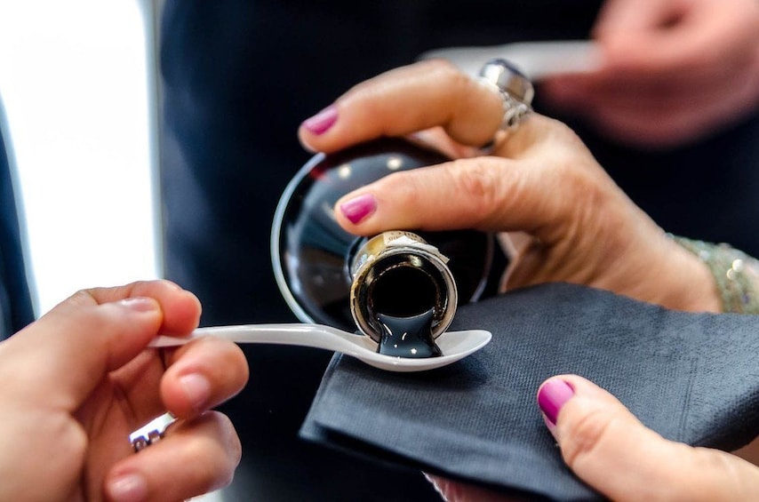 Show item 1 of 6. Woman pouring a spoon of balsamic vinegar for tasting on a tour in Modena