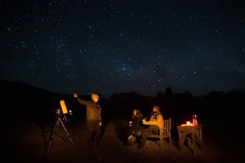 Discover the cosmos with our guide, telescope in focus, as you unwind on a bench with a hot drink in hand.