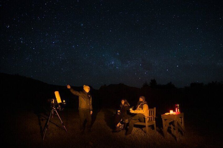 Discover the cosmos with our guide, telescope in focus, as you unwind on a bench with a hot drink in hand.