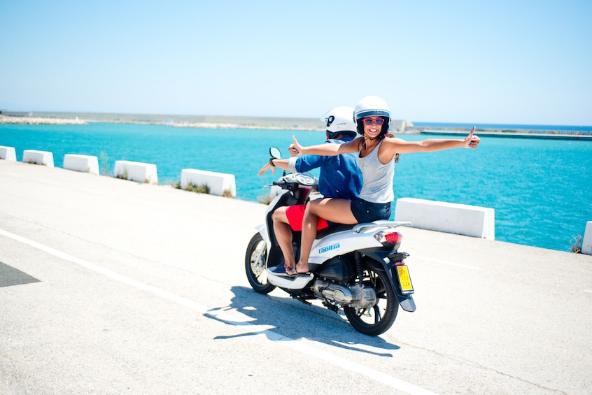 Ver elemento 4 de 5. Woman has her thumbs up while riding on a scooter with her partner in Menorca